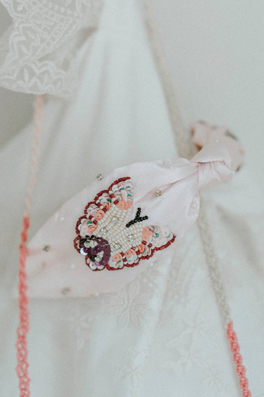 Girl holding a blush pink butterfly headband with beaded detailing, styled in front of a vintage mirror in a lace dress

Close-up of child's hands holding a pink satin headband with intricate butterfly beadwork and pearl accents

Elegant butterfly headband with pastel beads and embroidery, perfect for flower girls, birthdays, or dress-up play