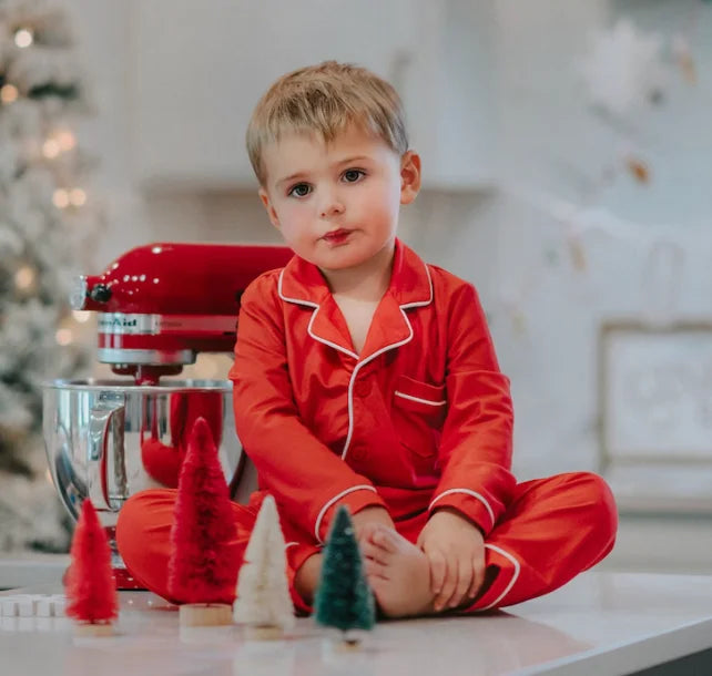 A young child is dressed in the buttery soft Unisex Pj's in Red from our Christmas Lounge Collection. The true Christmas red pajamas have a classic design.  They are piped with white trim.  The 2 piece pj set is perfect for photos and warm cozy holiday cheer. 