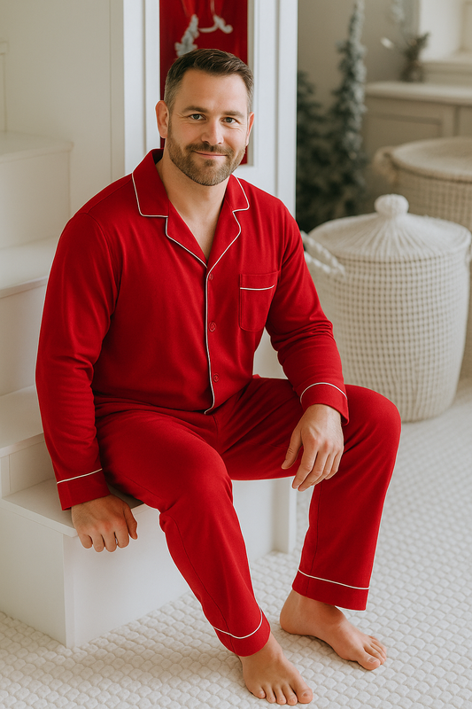 Man wearing red pajamas sitting on a white surface with a Christmas-themed room in the background.