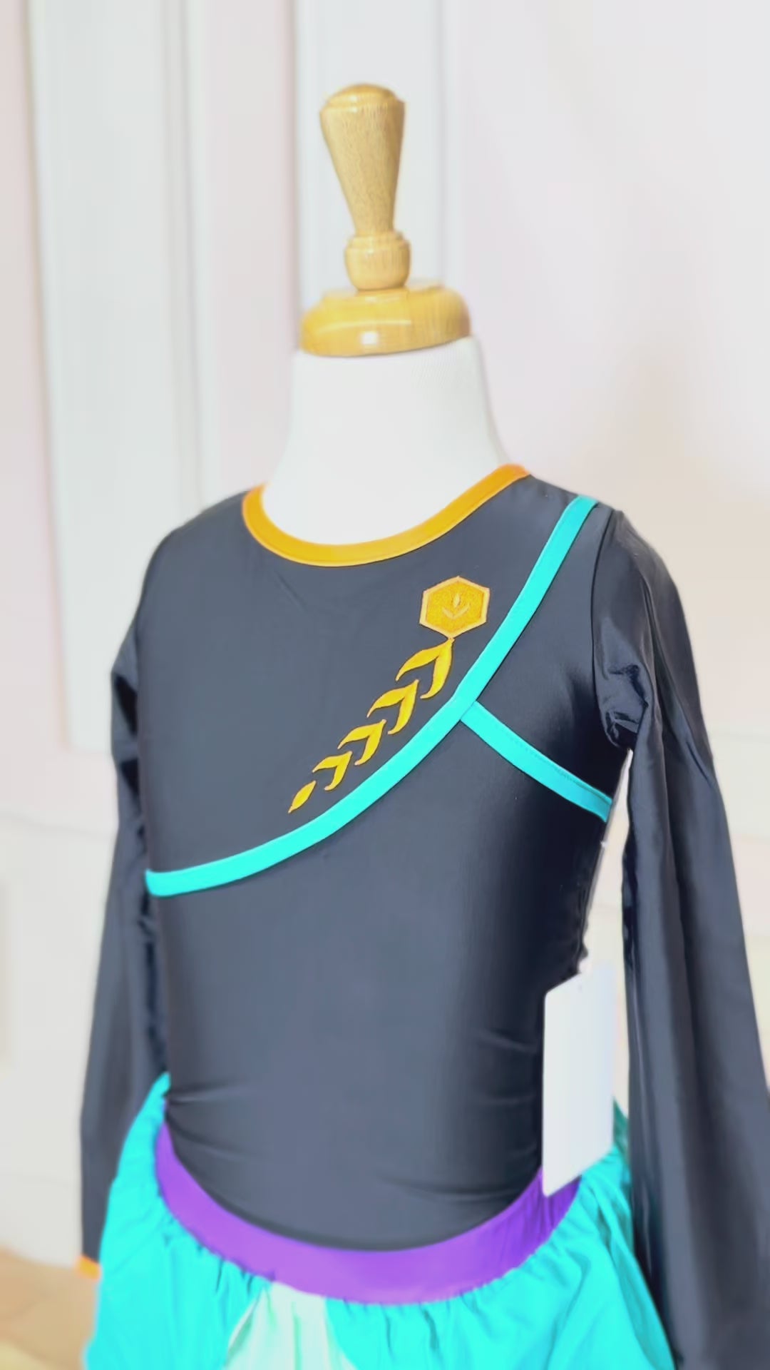 A young girl is wearing a 2 piece long sleeve rash guard swim set. The top is black with turquoise and goldenrod accents. The bottom has a turquoise ruffle over a mint teal skirt with goldenrod hem accent. 