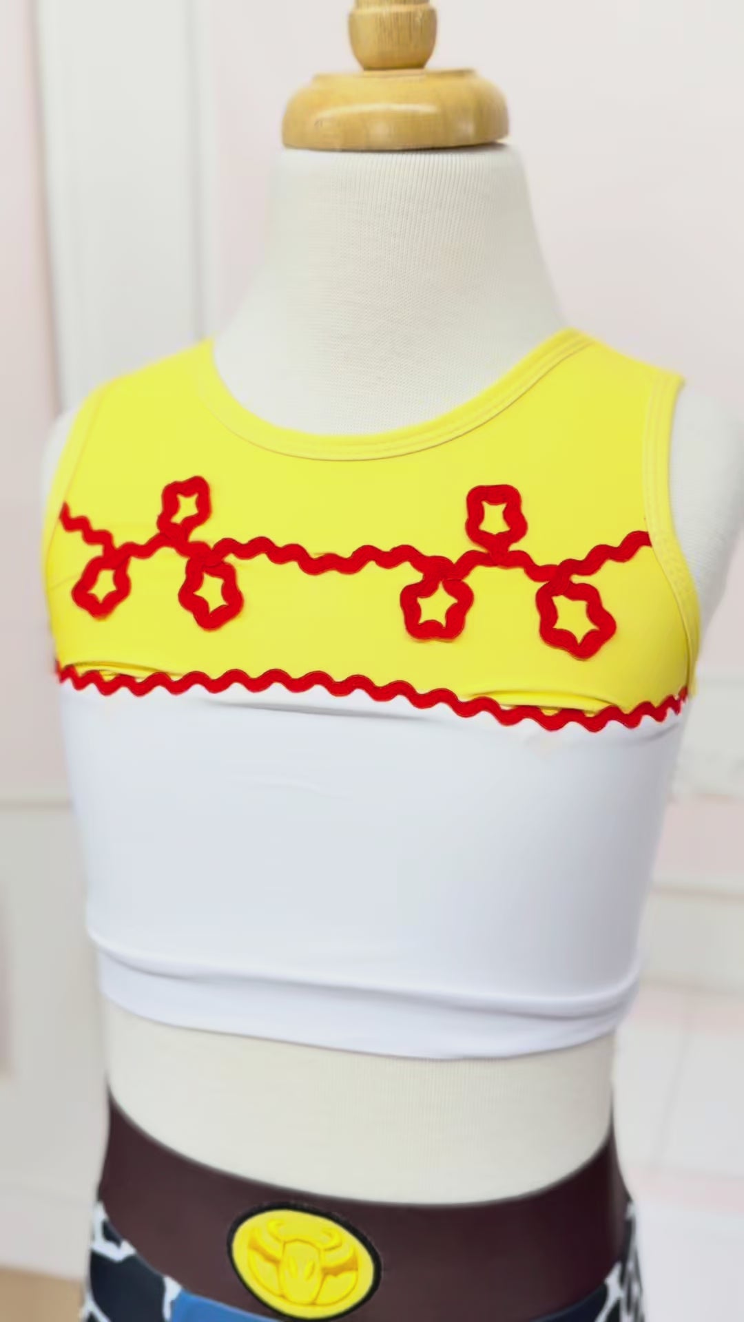 A 2 piece swim set.  The top is white with yellow on the upper chest.  Across the yellow is red scrolling rick rack.  The bottoms are a faux denim with black and white cow print panels. 