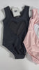 A young girl is wearing the Love Bug Leotard, a pink or black gymnastics outfit with an elegant heart cutout back. 