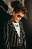 A child wears black and white face paint resembling a skeleton, with dark eye circles and a stitched mouth. Dressed in a comfortable poly-knit fabric faux jacket over "The Pumpkin King Shirt," which features a small embroidered bat motif. 