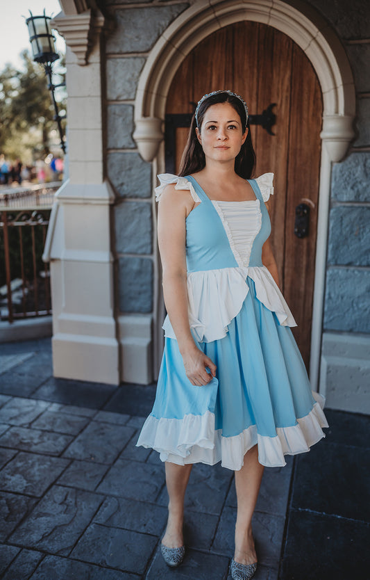 Eden is wearing our adult Cinderella Twirl dress.  The light blue dress has white ruffles on top of the blue straps. There is a white and blue bodice with a white peplum detail over the skirt. The light blue twirl skirt has a white ruffle hem. 