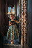 A young girl is wearing a Portrait Collection Coronation Ice Princess Gown inspired by Princess Anna from the movie "Frozen." The dress showcases a black velvet bodice with custom embroidery and a skirt adorned with green and gold accents. The skirt is shimmering in shades of green with embroidered designs along the panels.  There is tulle with cotton lining underneath to add fullness to the skirt. 