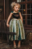 A young girl is wearing a Portrait Collection Coronation Ice Princess Gown inspired by Princess Anna from the movie "Frozen." The dress showcases a black velvet bodice with custom embroidery and a skirt adorned with green and gold accents. The skirt is shimmering in shades of green with embroidered designs along the panels.  There is tulle with cotton lining underneath to add fullness to the skirt. 