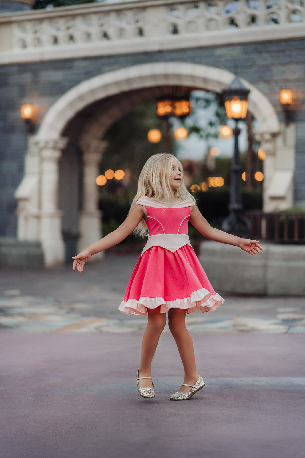 A young girl is wearing an all cotton bright pink princess twirl dress. The neckline has nude mesh and light pink sits off the shoulder.  The bright pink bodice has light pink piping and leads into a light pink handkerchief band.  The skirt is flowy and bright pink.  A light pink ruffle at the hem line adds a beautiful twirl. 