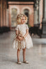 A young girl stands dressed in the Evangeline Frock in Antique Ivory. Ivory tulle and lace dress features a built in petticoat for an extra full skirt and retro silhouette. The dress has cotton slip lining.