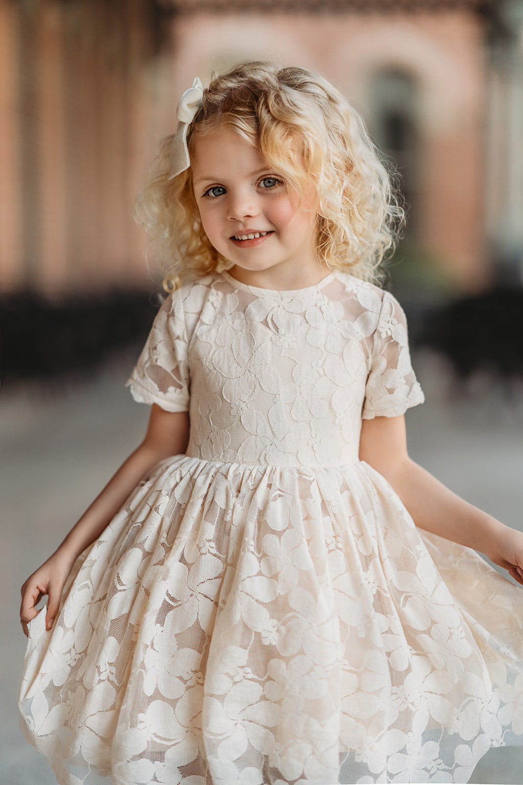 A young girl stands dressed in the Evangeline Frock in Antique Ivory. Ivory tulle and lace dress features a built in petticoat for an extra full skirt and retro silhouette. The dress has cotton slip lining.