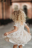 A young girl stands dressed in the Evangeline Frock in Antique Ivory. Ivory tulle and lace dress features a built in petticoat for an extra full skirt and retro silhouette. The dress has cotton slip lining.