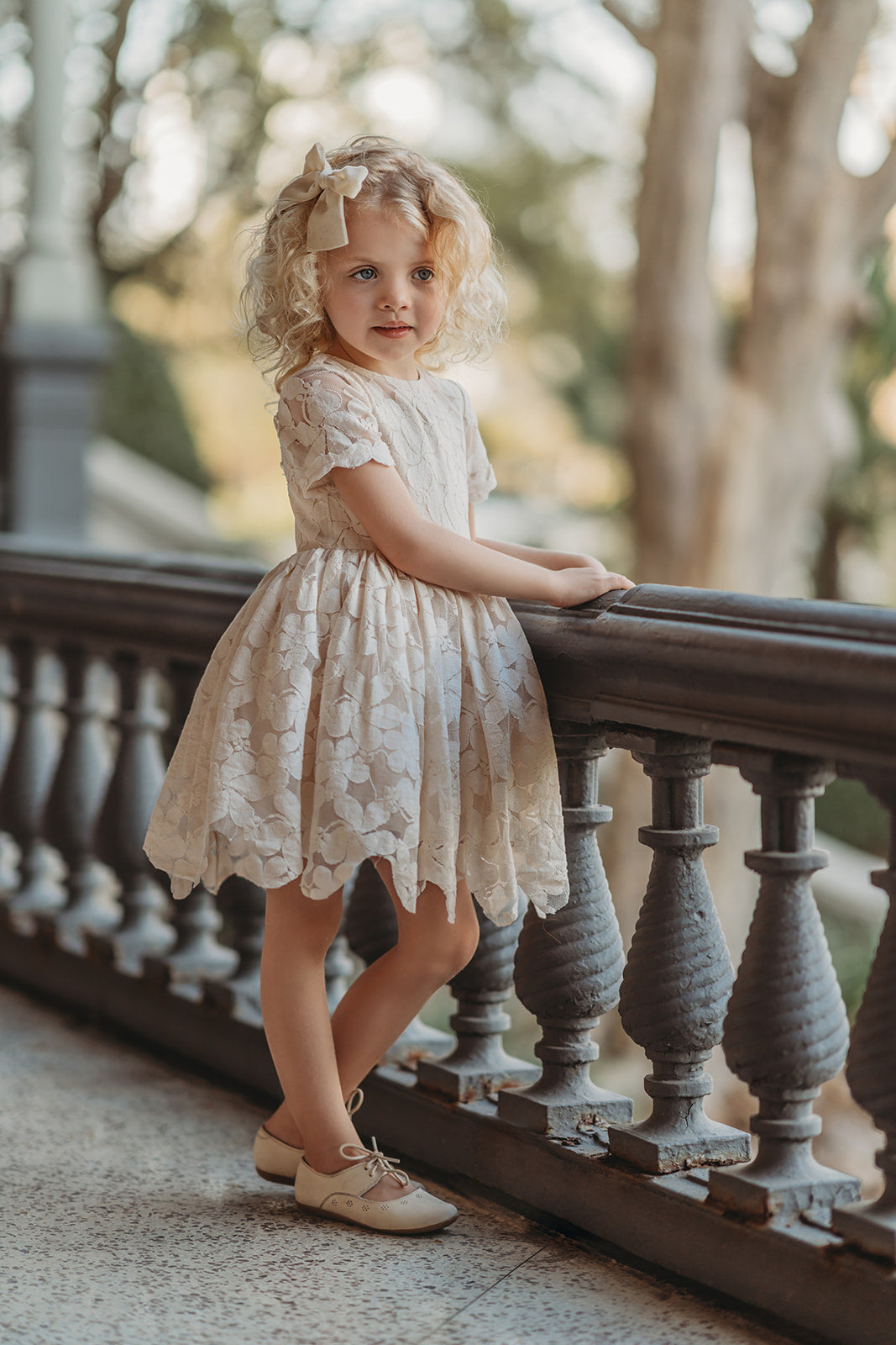 A young girl stands dressed in the Evangeline Frock in Antique Ivory. Ivory tulle and lace dress features a built in petticoat for an extra full skirt and retro silhouette. The dress has cotton slip lining.