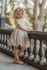 A young girl stands dressed in the Evangeline Frock in Antique Ivory. Ivory tulle and lace dress features a built in petticoat for an extra full skirt and retro silhouette. The dress has cotton slip lining.