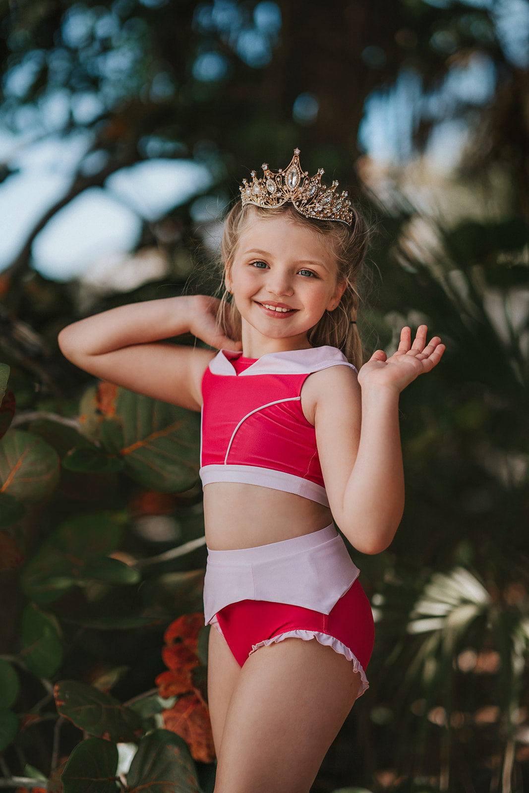 A young girl is wearing a pink 2 piece swimsuit.  The Sleeping Beauty swim set has a pink collar that resembles a ballgown.  The top has light pink piping and trim.  The modest bottoms have a pink overlay and ruffles on the legs. 