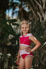 A young girl is wearing a pink 2 piece swimsuit.  The Sleeping Beauty swim set has a pink collar that resembles a ballgown.  The top has light pink piping and trim.  The modest bottoms have a pink overlay and ruffles on the legs. 