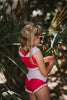 A young girl is wearing a pink 2 piece swimsuit.  The Sleeping Beauty swim set has a pink collar that resembles a ballgown.  The top has light pink piping and trim.  The modest bottoms have a pink overlay and ruffles on the legs. 