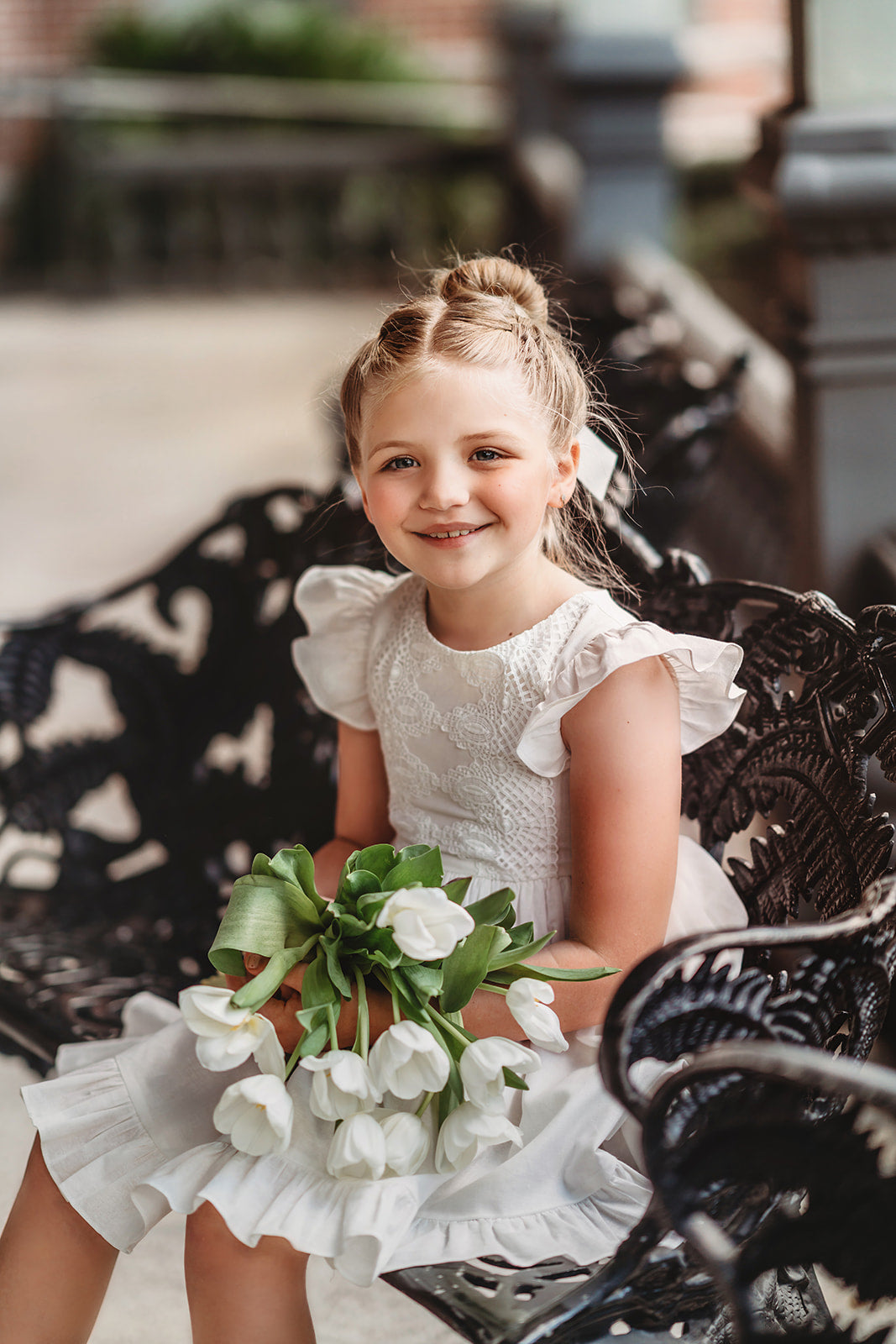 A young girl is wearing the Ethel Fancy Pinafore in Soft White with ruffled sleeves. There is a matching lace overlay on the bodice.  A pettiskirt can be added underneath the dress for fullness. 