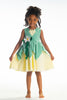 A young girl poses in the Frog Princess Twirl Dress . She wears a green and yellow dress with a magnolia accent at the waist. The light green top and leaf shaped skirt are overlayed on a light yellow skirt with white eyelet trim at the bottom.  The dress is sleeveless and a comfortable cotton. 