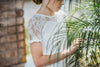 A young girl stands dressed in the Evangeline Frock in White. White tulle and lace dress features a built in petticoat for an extra full skirt and retro silhouette. The dress has cotton slip lining.