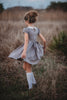 A young girl is wearing a grey Wizard Girl Twirl Dress with a striped yellow and brick red tie. The twirl dress has a white collar, short puff sleeves and a tie in the back at the waist. 