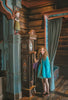 A young girl twirls in the vibrant Older Ice Princess Sister Set Style C dress, embellished with teal and purple accents. The removable cape is purple and teal with brown gold trim. The short sleeves feature a golden brown design.