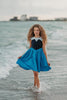 A young girl is wearing a Kiss the Girl Mermaid Dress from The Fairy Godmother Collection, featuring a navy bodice and light blue cap sleeves. The dress skirt is a bight cerulean blue. The material is woven cotton. 