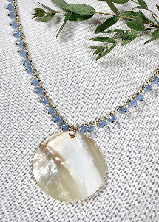 A golden chain with blue crystal accents.  In the center a large mother of pearl disc. 