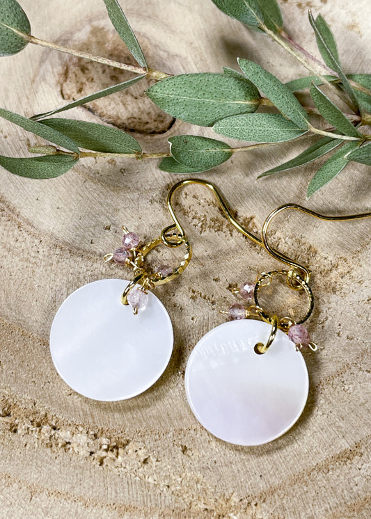 A golden hook with golden hoop and small crystal charms attaches to a large mother of pearl disc. 