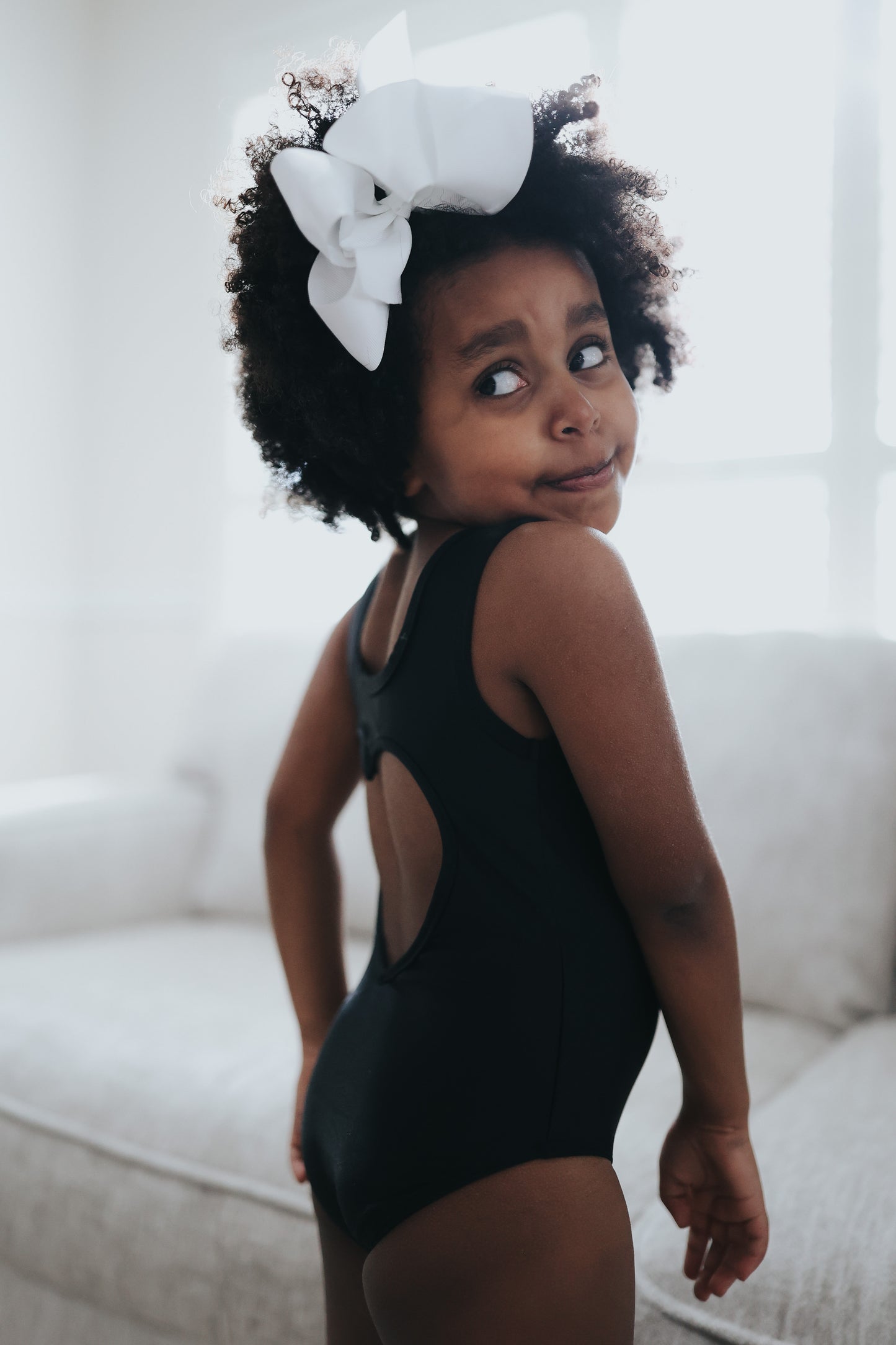 A young girl is wearing the Love Bug Leotard, a black gymnastics outfit with an elegant heart cutout back. 