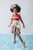 A young girl is wearing the Polynesian Princess Twirl Dress, which features beige and cream fabric accented by a red waistband and decorative floral embroidery.  There is a lace accent on the chest and ruffles on the top of the straps.  There is a ruffle on the hem and a tie on the side of the dress. Perfect for an adventurous princess. 