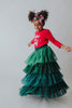 A young girl is wearing a long skirt in layers of green tulle.  The ruffles  cascade from green to evergreen.  There are 4 colors of green and 7 layers of tulle with a cotton liner for comfort. 