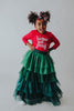 A young girl is wearing a long skirt in layers of green tulle.  The ruffles  cascade from green to evergreen.  There are 4 colors of green and 7 layers of tulle with a cotton liner for comfort. 