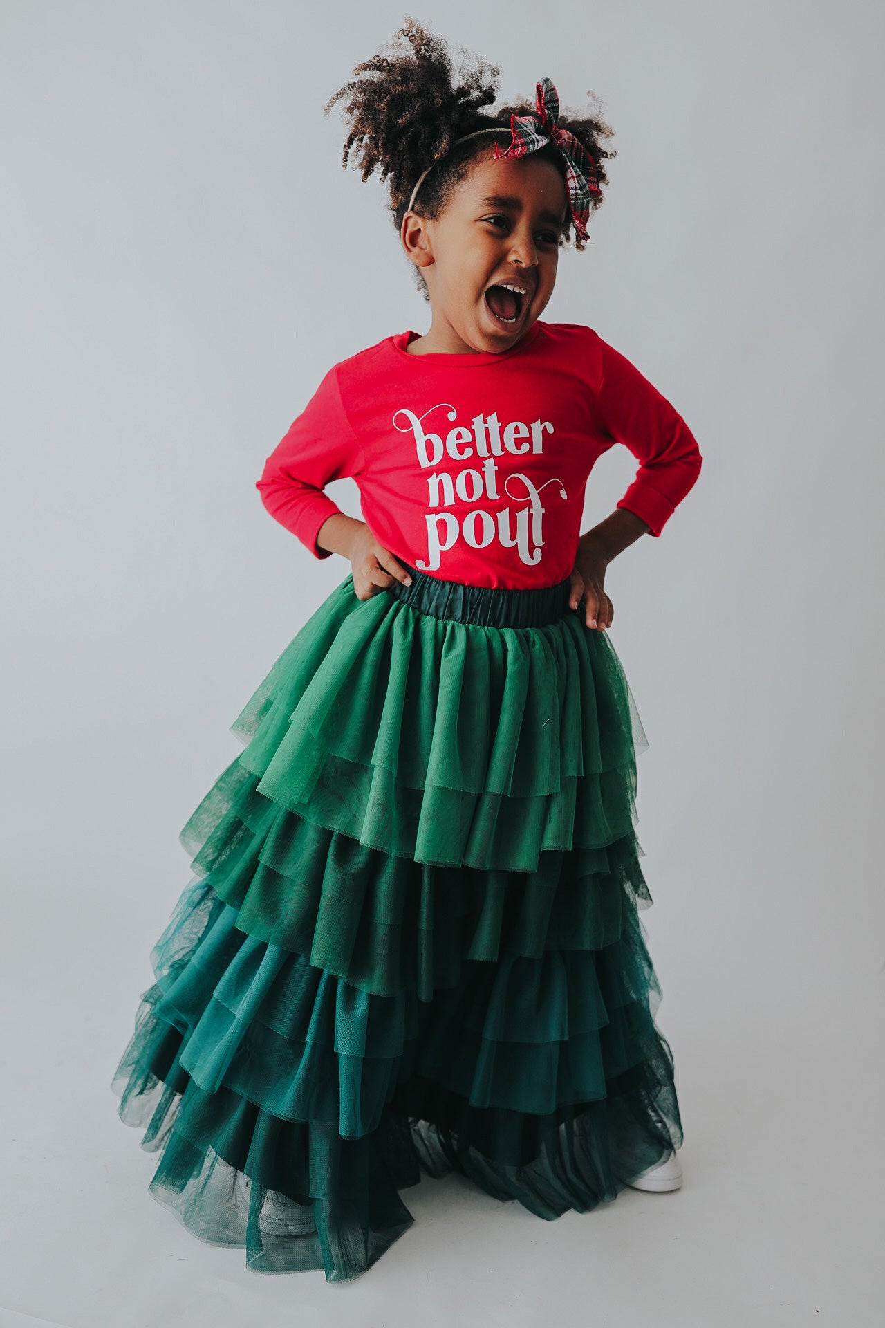 A young girl is wearing a long skirt in layers of green tulle.  The ruffles  cascade from green to evergreen.  There are 4 colors of green and 7 layers of tulle with a cotton liner for comfort. 