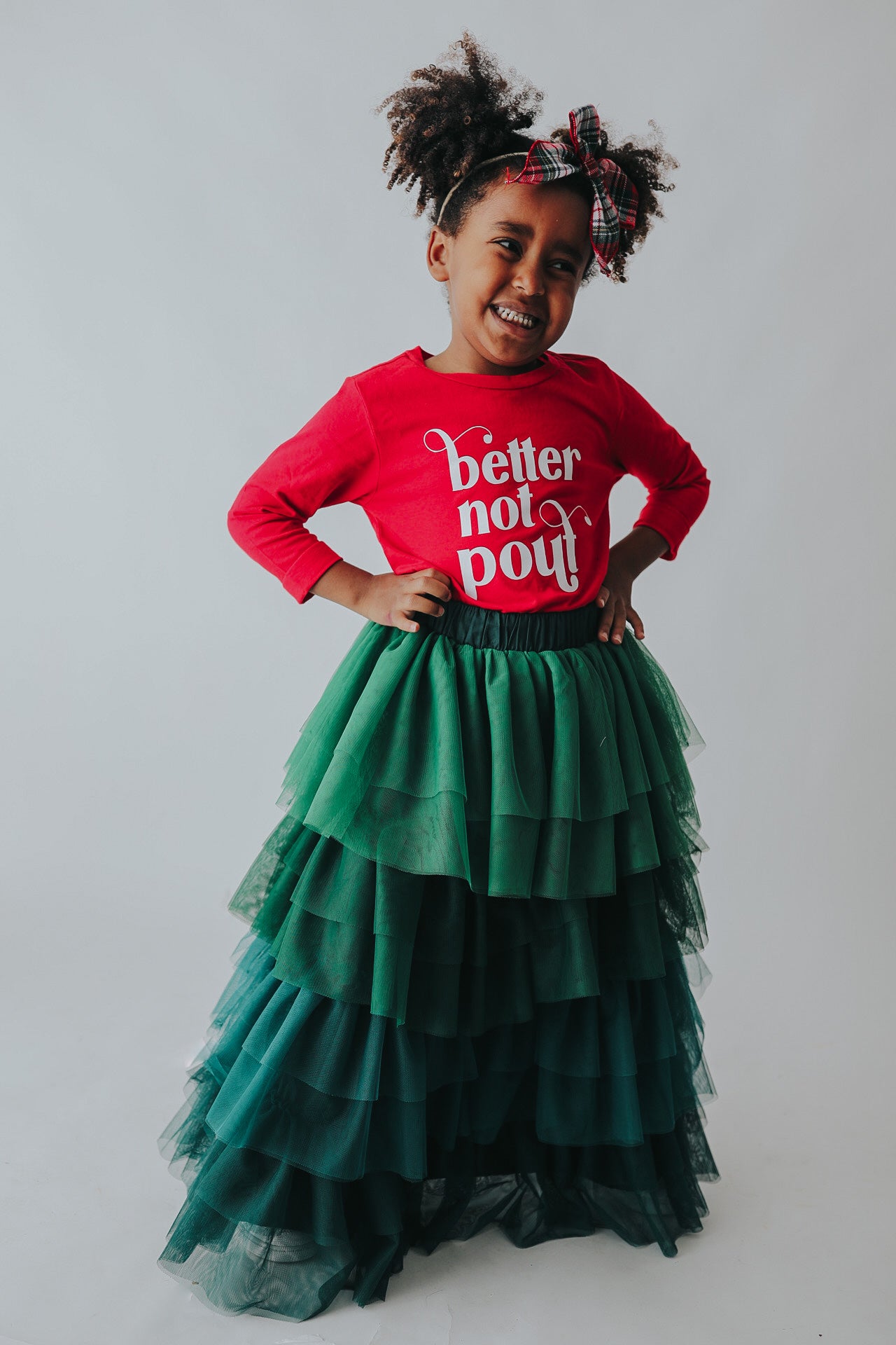 A young girl is wearing a long skirt in layers of green tulle.  The ruffles  cascade from green to evergreen.  There are 4 colors of green and 7 layers of tulle with a cotton liner for comfort. 