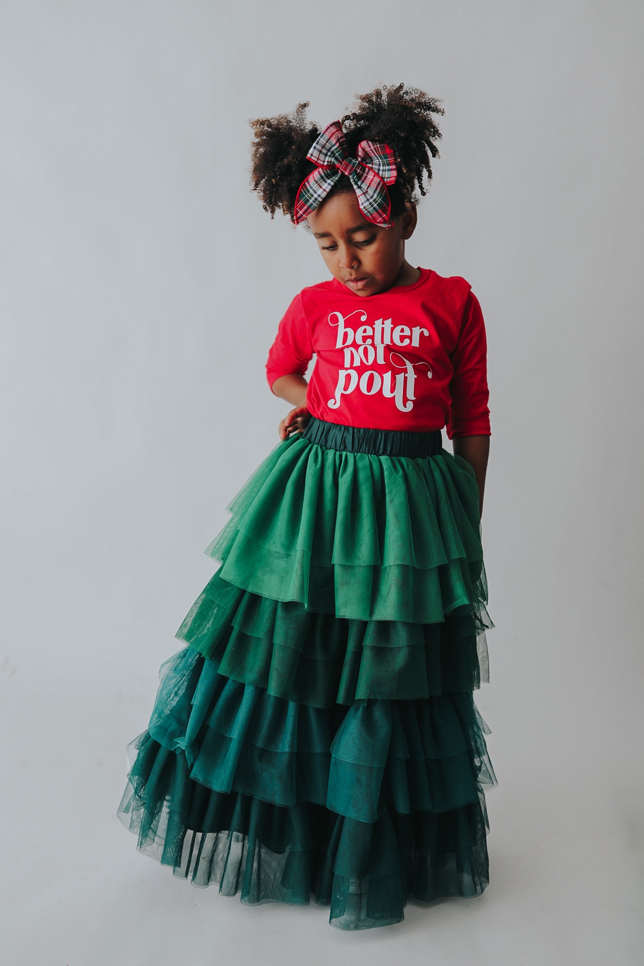 A young girl is wearing a long skirt in layers of green tulle.  The ruffles  cascade from green to evergreen.  There are 4 colors of green and 7 layers of tulle with a cotton liner for comfort. 