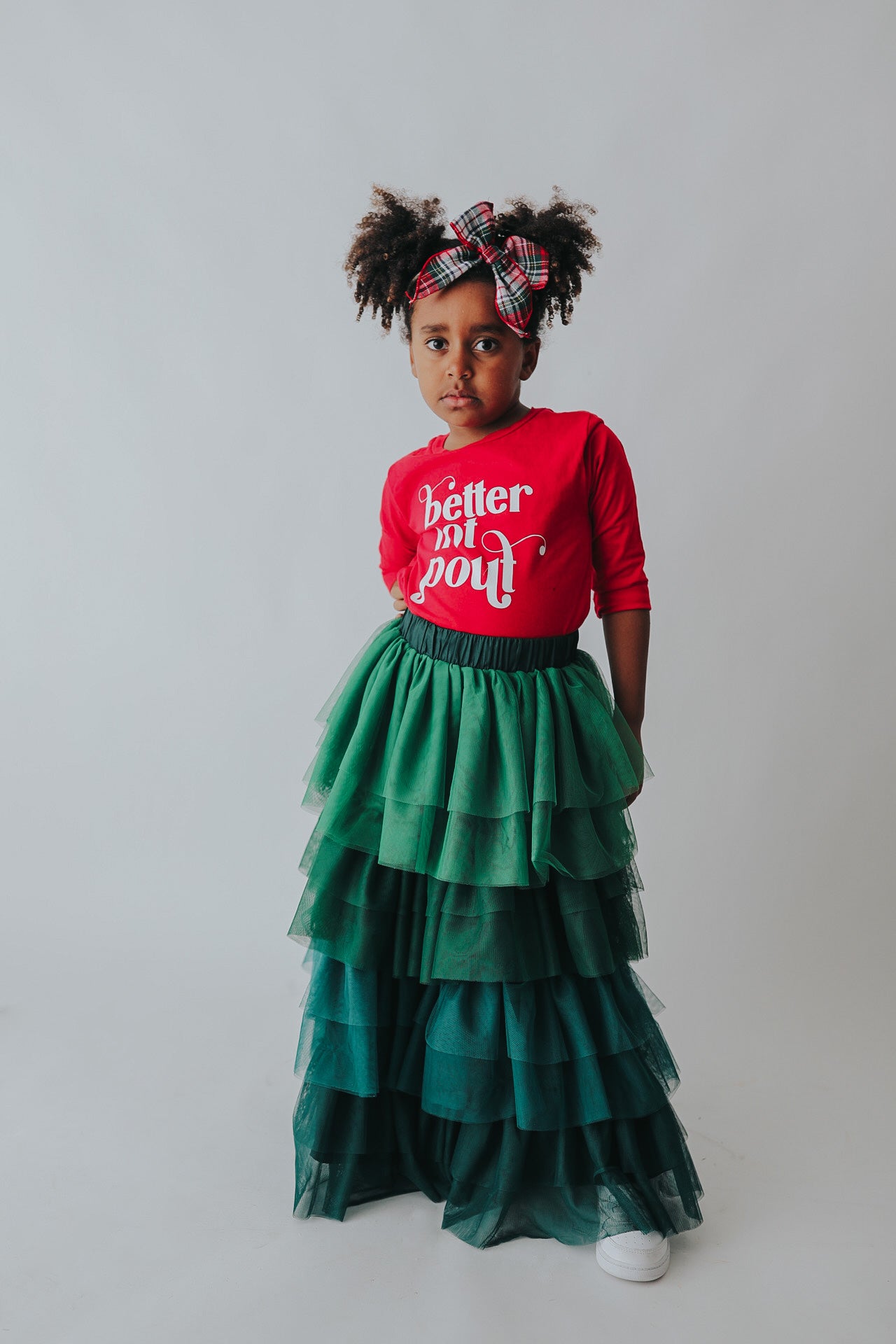 A young girl is wearing a long skirt in layers of green tulle.  The ruffles  cascade from green to evergreen.  There are 4 colors of green and 7 layers of tulle with a cotton liner for comfort. 