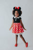 A young girl is wearing the Miss Mouse Twirl Dress, which features a black bodice, puff sleeves and a white collar.  Three white buttons decorate the center. The skirt is red with white polka dots and white eyelet lace trim.