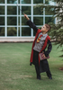 A young boy dressed in the Wizard Ensemble, featuring a red and yellow striped tie, and a black cotton jersey knit robe reminiscent of the Harry Potter series. The robe is lined with brick red and there is a logo sewn over the left chest. 