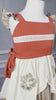  The Polynesian Princess Twirl Dress, which features beige and cream fabric accented by a red waistband and decorative floral embroidery.  There is a lace accent on the chest and ruffles on the top of the straps.  There is a ruffle on the hem and a tie on the side of the dress. Perfect for an adventurous princess. 