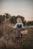 A young child wearing The Fairy Godmother Collection Sleeping Beauty dress with a white collar and lace trim. The black bodice and light brown skirt are woven cotton.  The dress structure is fitted in the top and flares out as the waist. 