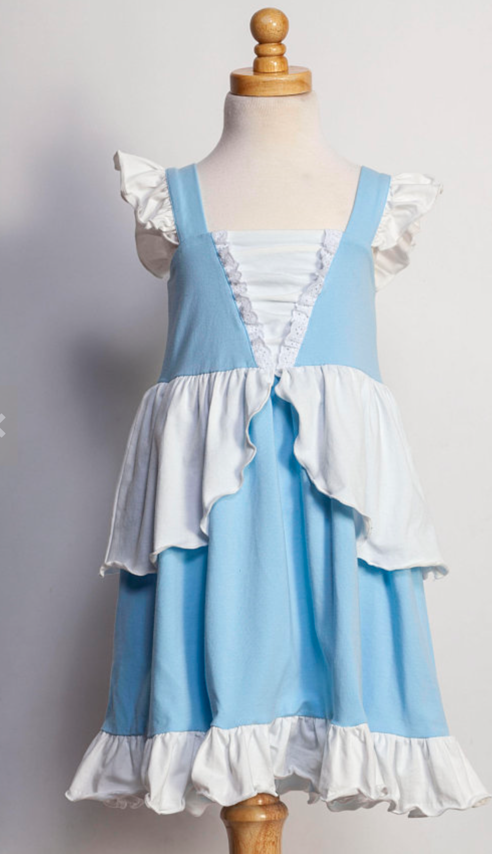 A young girl in an "Our Original Cinderella Twirl Dress" stands near a castle.  The dress has a white flutter ruffle on the straps. There is a white skirt ruffle that overlays the blue twirl skirt. The soft cotton material is comfortable and breathable. 