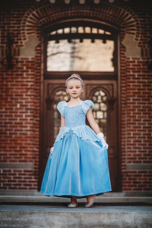 A young girl stands in a light blue gown.  The chiffon puff sleeves lead into a light blue lace bodice.  There is a small chiffon bustle ruffle over a stretch velour skirt.  The skirt is lined with tulle and cotton for fullness. 