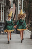 A young girl stands wearing the Smiling Elf Dress, adorned with yellow embroidery, a white collar, and a yellow hem. She also sports a matching yellow cone hat.