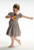 A young girl is wearing a grey Wizard Girl Twirl Dress with a striped yellow and brick red tie. The twirl dress has a white collar, short puff sleeves and a tie in the back at the waist. 