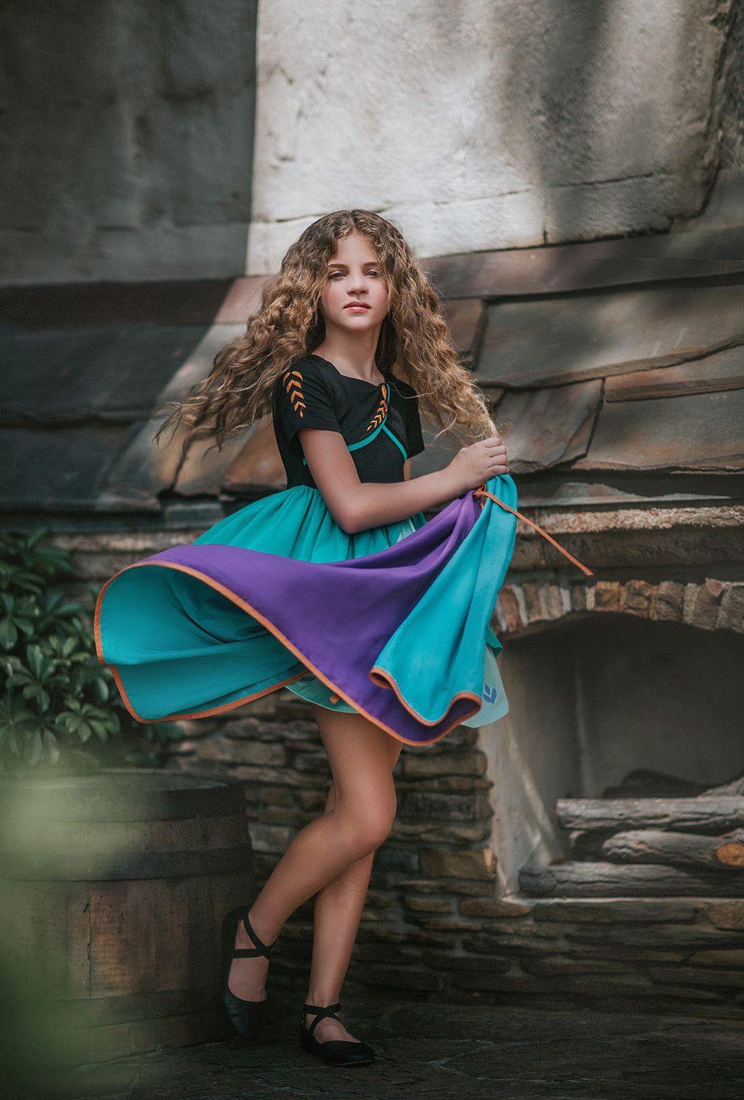 A young girl twirls in the vibrant Older Ice Princess Sister Set Style C dress, embellished with teal and purple accents. The removable cape is purple and teal with brown gold trim. The short sleeves feature a golden brown design.