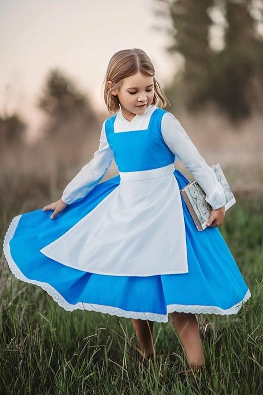 A young girl stands wearing the Red Rose Princess Village Dress from the Fairy Godmother Collection, reminiscent of Disney's Belle from "Beauty and the Beast." The white sleeves are long. The dress has a bight blue chest and skirt.  There is a white apron at the waist and white embroidery lace at the base. Dress is mid calf.
her 100% woven cotton dress to flare out. The background is softly blurred with trees and sky visible.