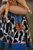 A young girl is wearing a Cowgirl Character Twirl Dress from the Toyland Collection. The sleeveless dress has a yellow and white bodice with red rick rack swirled across it.  The twirl skirt features a blue faux denim with black and white cow print and red rick rack trim. 