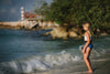 A young girl is wearing a 2 piece swim set.  The top is white with yellow on the upper chest.  Across the yellow is red scrolling rick rack.  The bottoms are a faux denim with black and white cow print panels. 