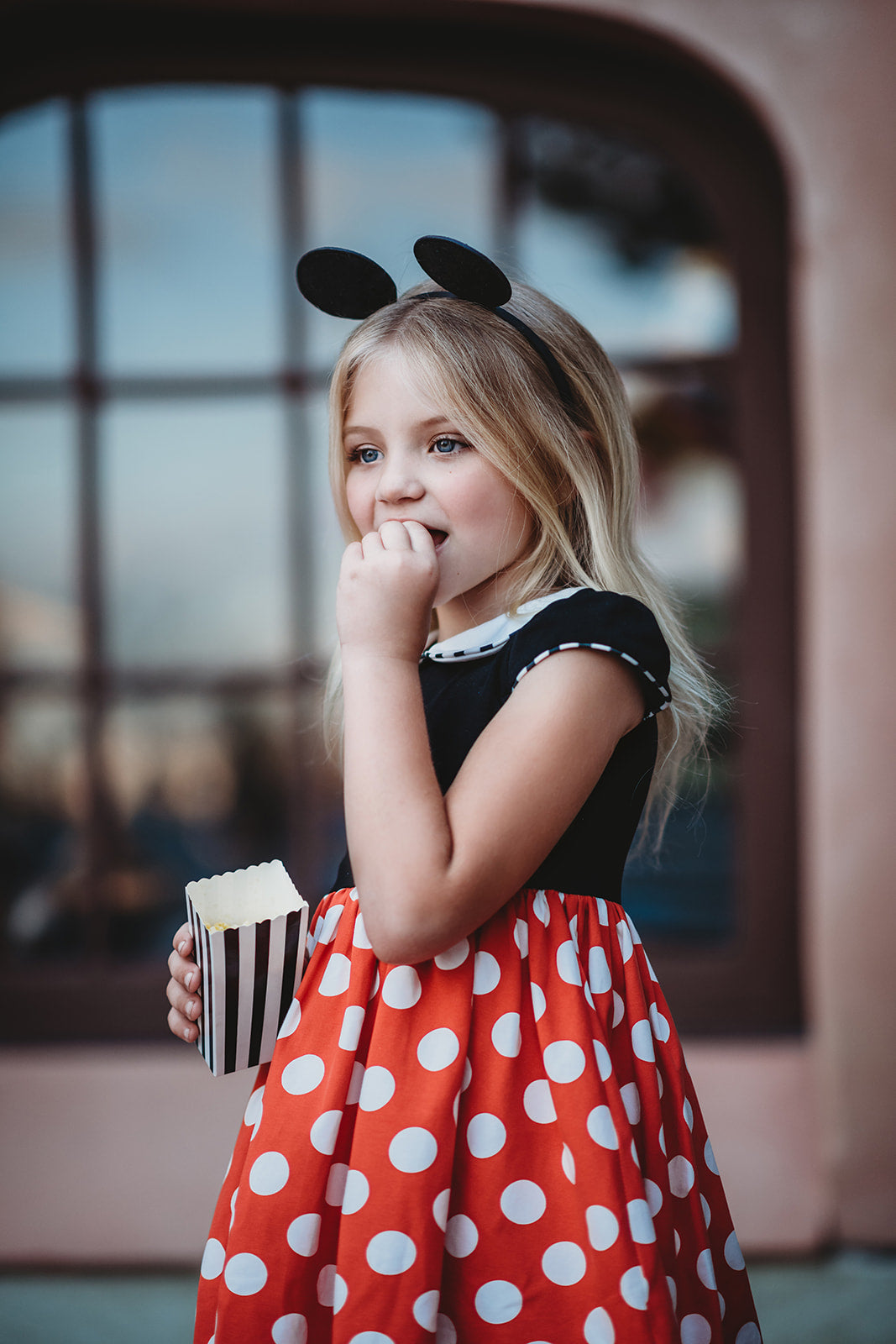 A young girl is wearing the Miss Mouse Twirl Dress, which features a black bodice, puff sleeves and a white collar.  Three white buttons decorate the center. The skirt is red with white polka dots and white eyelet lace trim.