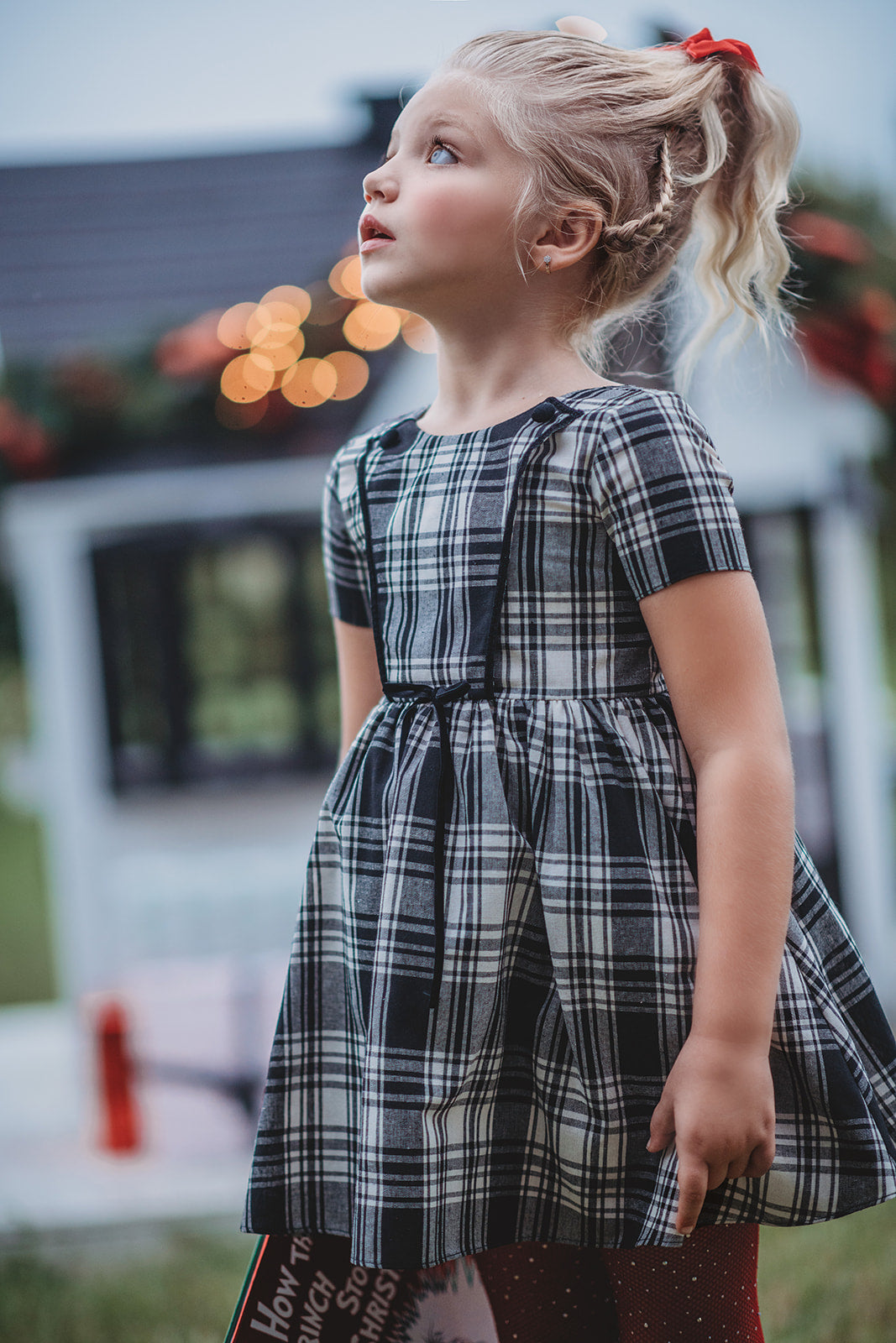 A young girl stands dressed in a black and white vintage plaid dress. The dress is mid thigh length and a sewn in pettiskirt add fullness to the bottom of the dress. 