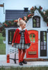 A young girl stands dressed in a black and white vintage plaid dress. A red velvet cape trimmed with white fur and a black bow are tied around her shoulders. The dress is mid thigh length and a sewn in pettiskirt add fullness to the bottom of the dress. 